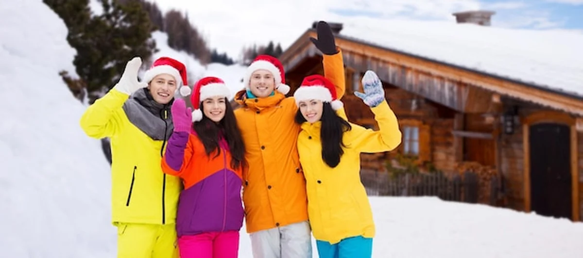 Szczęśliwi przyjaciele w czapkach Mikołaja i kombinezonach narciarskich na śniegu