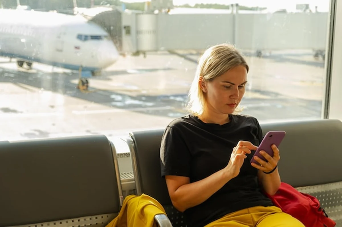 Kobieta na lotniskowym terminalu surfuje w smartfonie i telefonie komórkowym